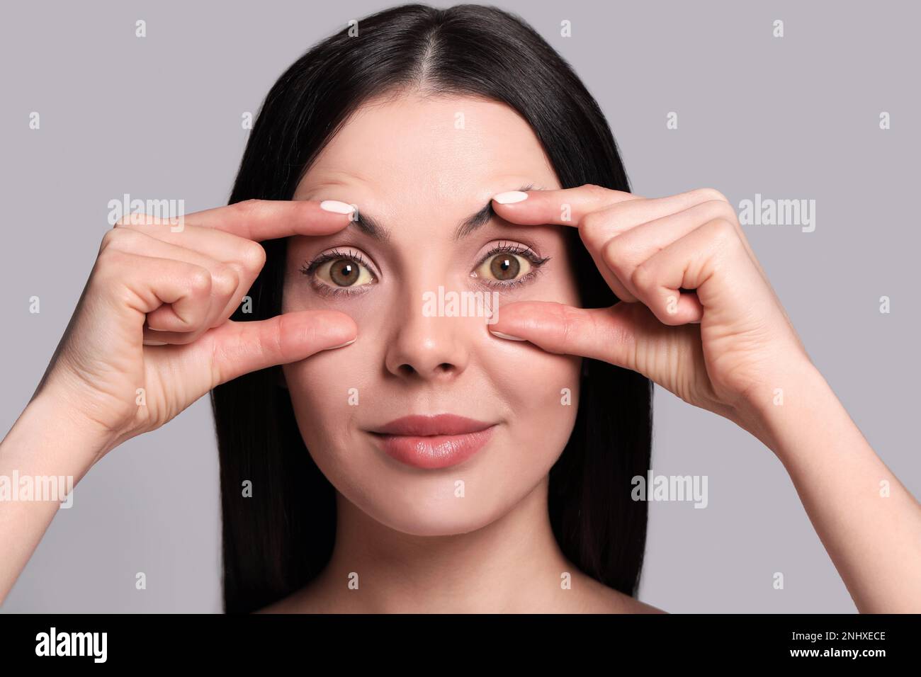 Femme vérifiant son état de santé sur fond gris. Yeux jaunes comme symptôme de problèmes avec le foie Banque D'Images
