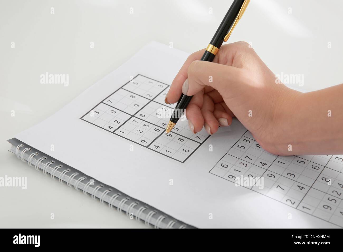 Femme résolvant sudoku puzzle à table blanche, gros plan Banque D'Images