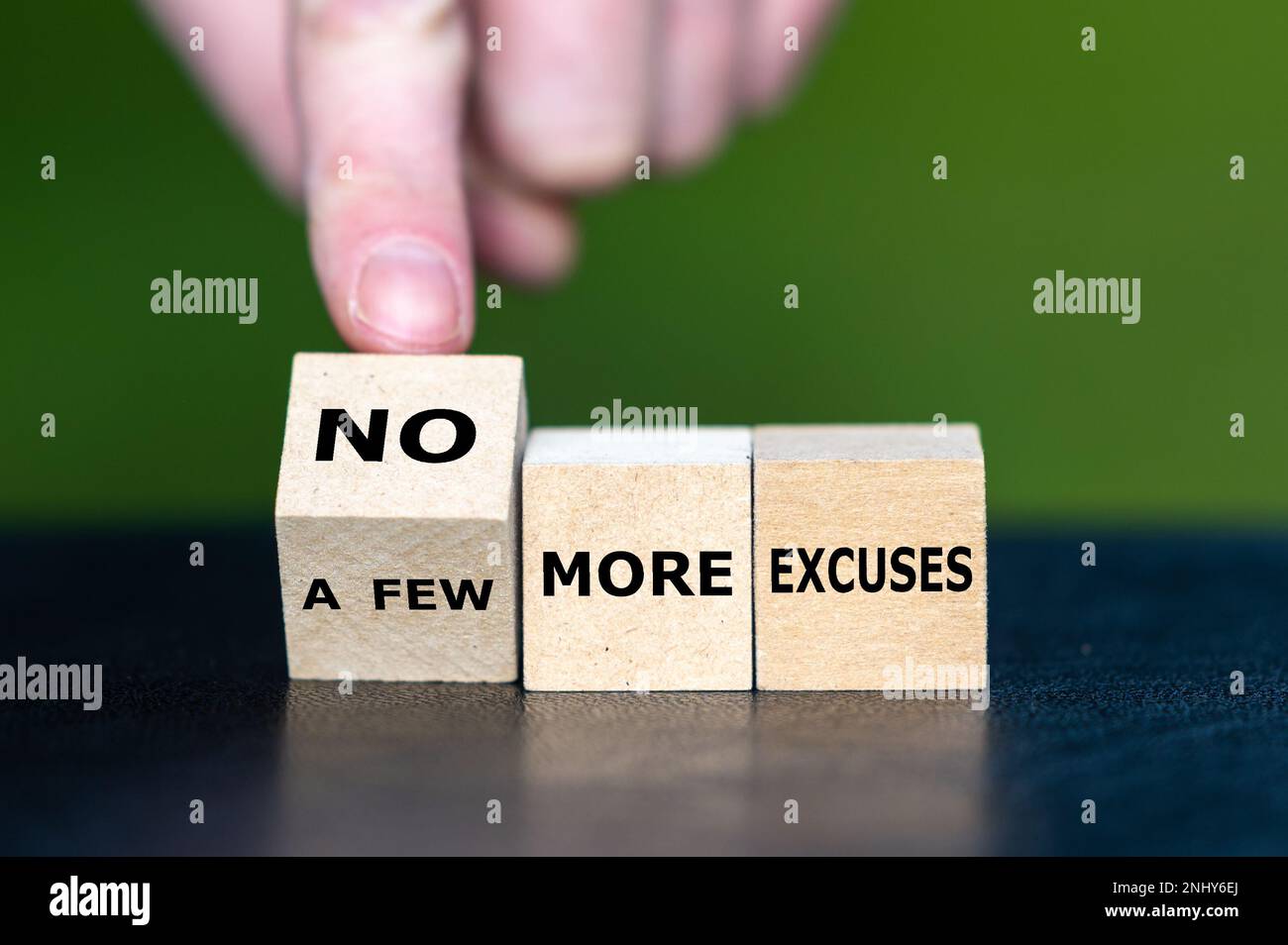 La main tourne un cube en bois et change l'expression 'un peu plus d'excuses' à 'plus d'excuses'. Banque D'Images
