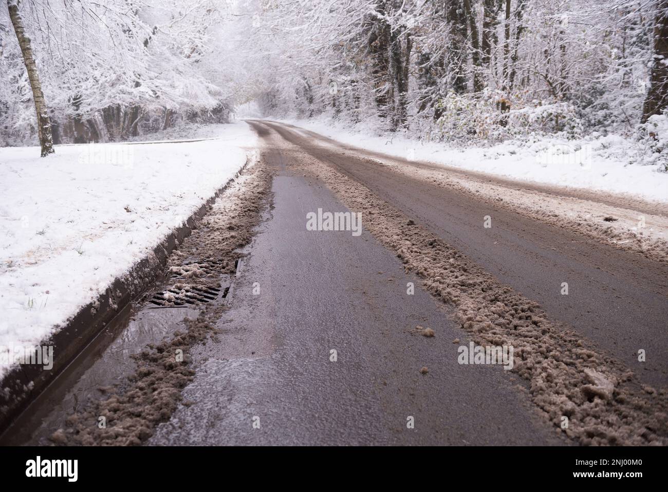 La propagation du sel sur les routes contribue à faire fondre la nouvelle chute de neige, mais la neige fondante commence à s'accumuler sur le trottoir et bloque les drains Banque D'Images