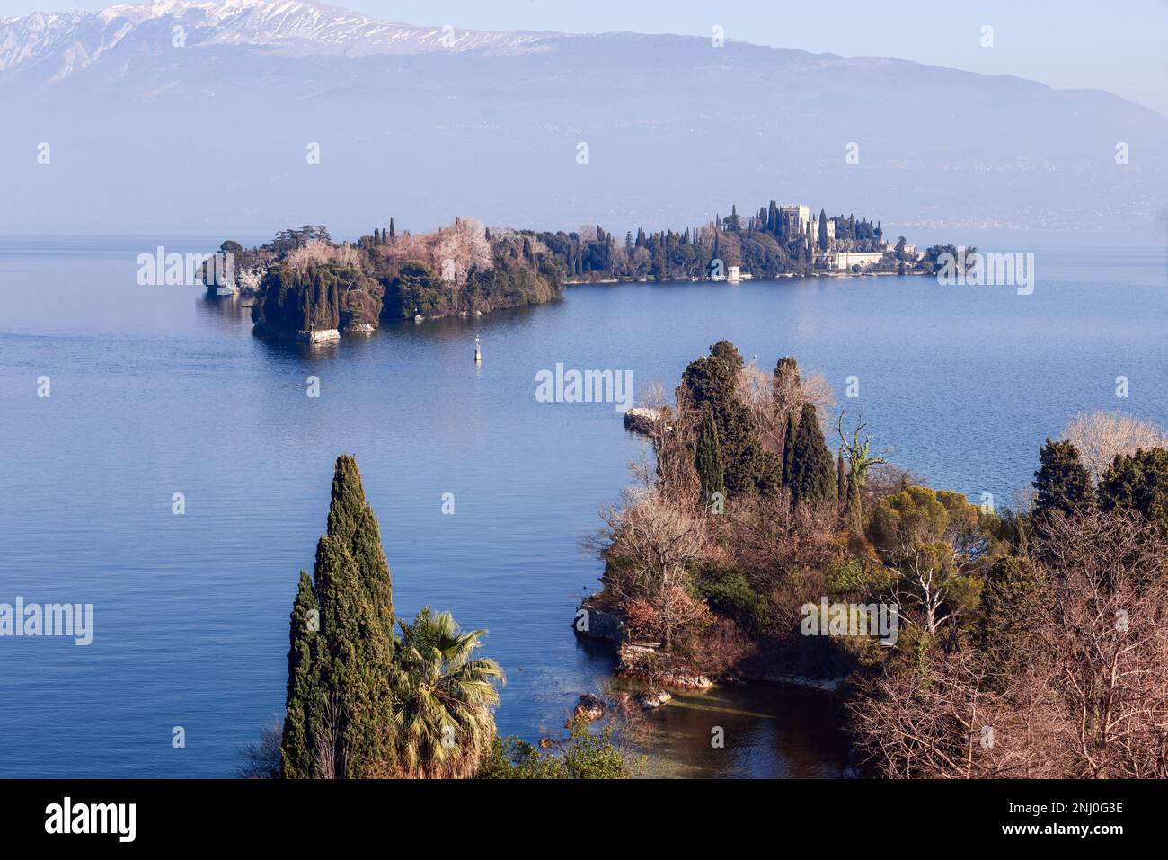 Isola del Garda et sa villa néo-gothique pâle se trouvent dans le lac bleu et calme du lac de Garde sous les montagnes alpines enneigées, Lombardie, Italie. Banque D'Images