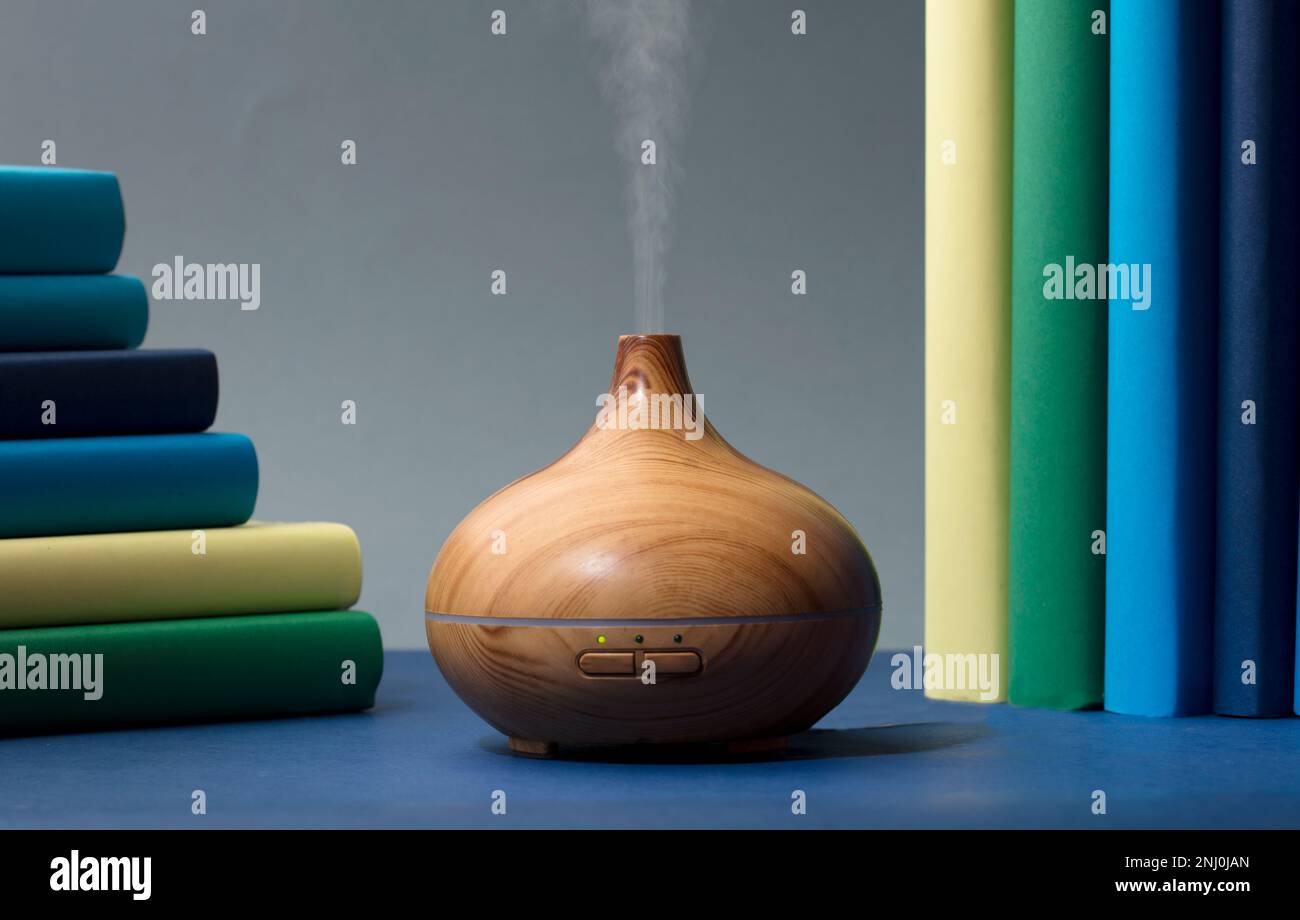 Vaporisateur en bois avec vapeur d'huiles naturelles, avec différentes gammes de bleu, jaune, vert, sur la table grise dans le salon Banque D'Images