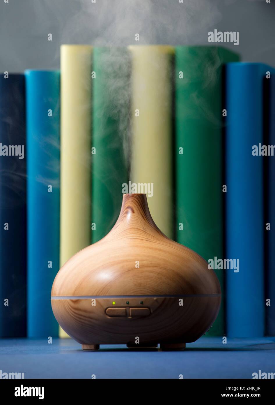 Vaporisateur en bois avec vapeur d'huiles naturelles, avec différentes gammes de bleu, jaune, vert, sur la table grise dans le salon Banque D'Images
