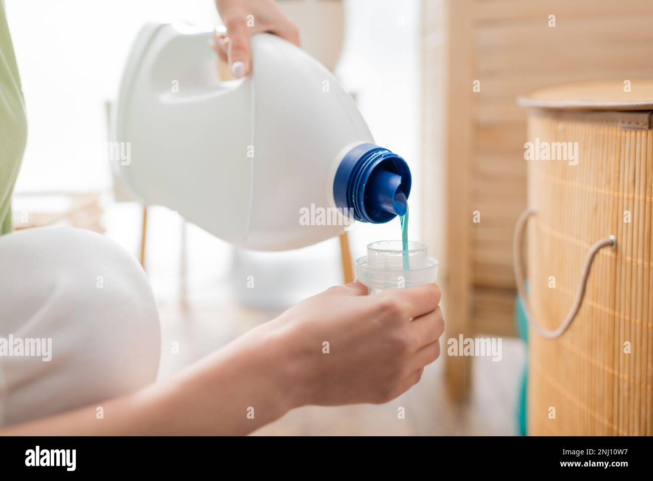 Vue rognée de la femme versant le liquide de lavage dans le capuchon de la bouteille dans la buanderie, image de stock Banque D'Images