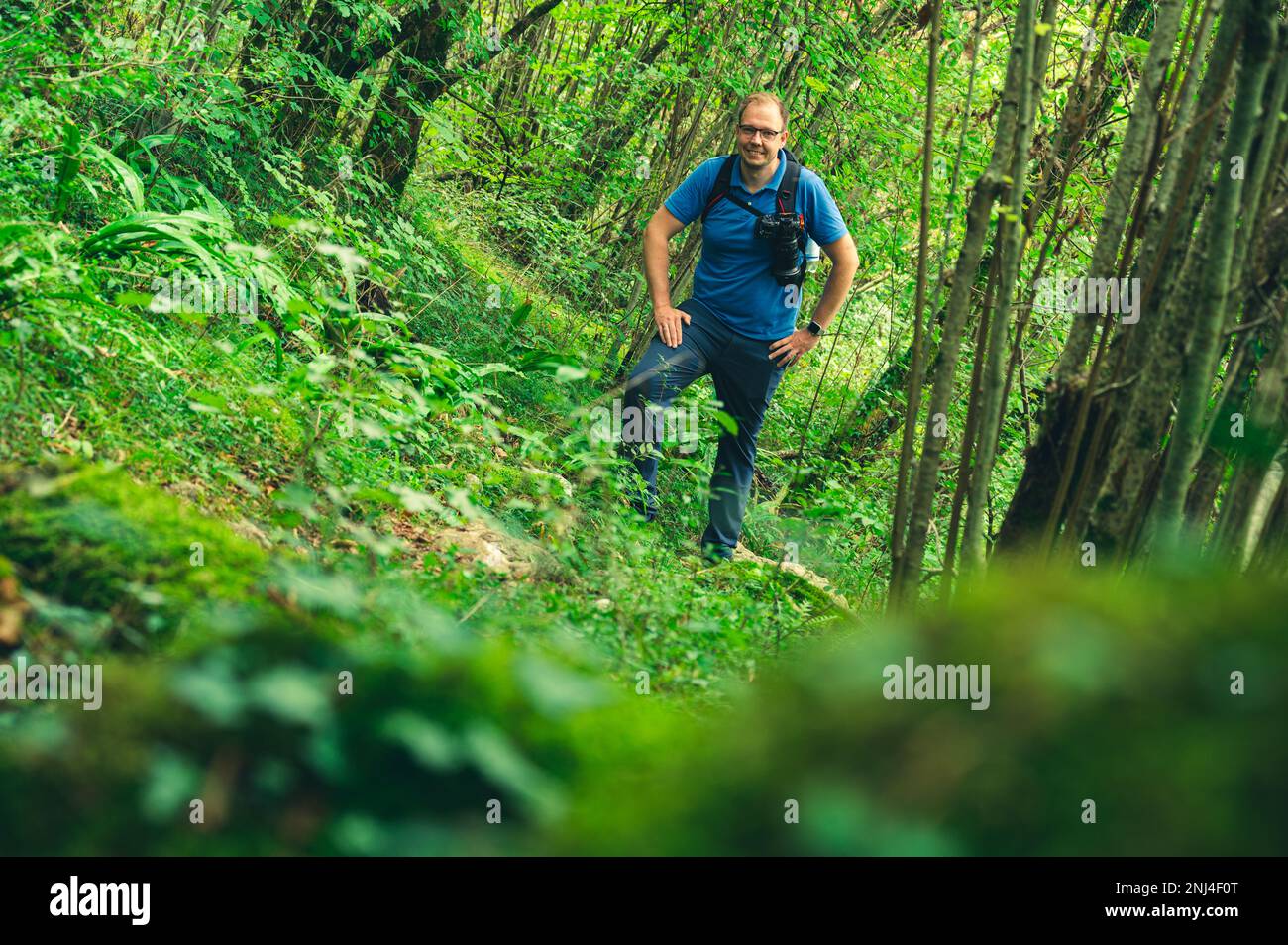 Photographe souriant avec sac à dos et appareil photo sur une pente raide dans la jungle Banque D'Images