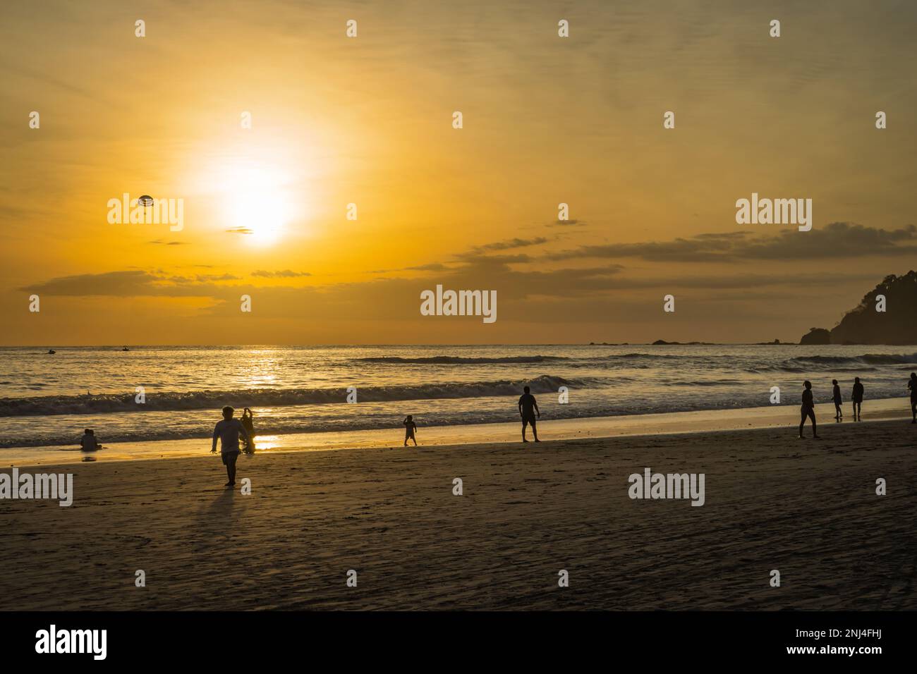 Coucher de soleil sur la plage le long de la côte Pacifique du Costa Rica avec parachute ascensionnel en montgolfière avec deux nageurs surplombant l'océan Banque D'Images