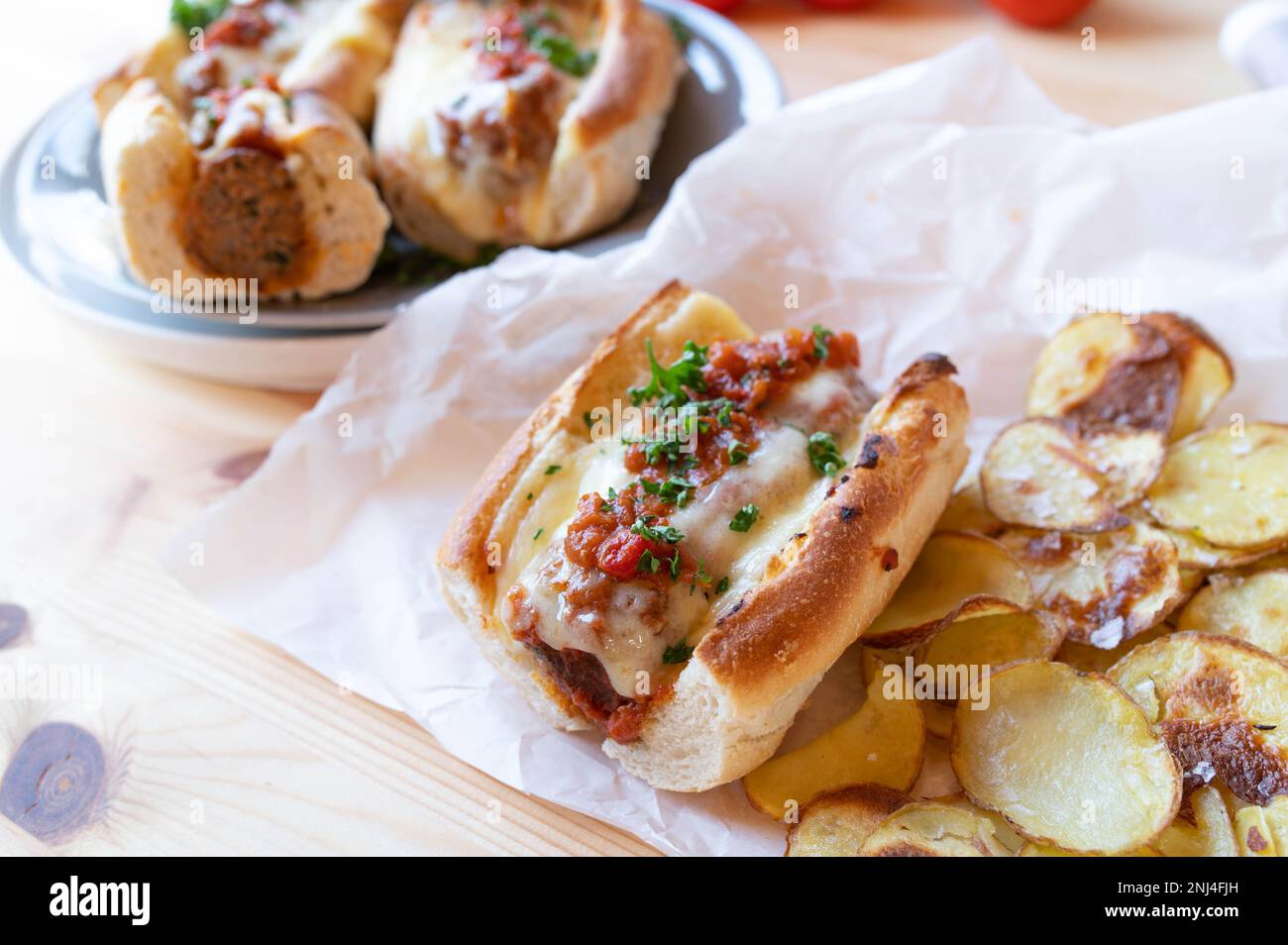 Sandwich meatball avec sauce tomate, fromage fondu et chips de pommes de terre faites maison sur la table de cuisine Banque D'Images
