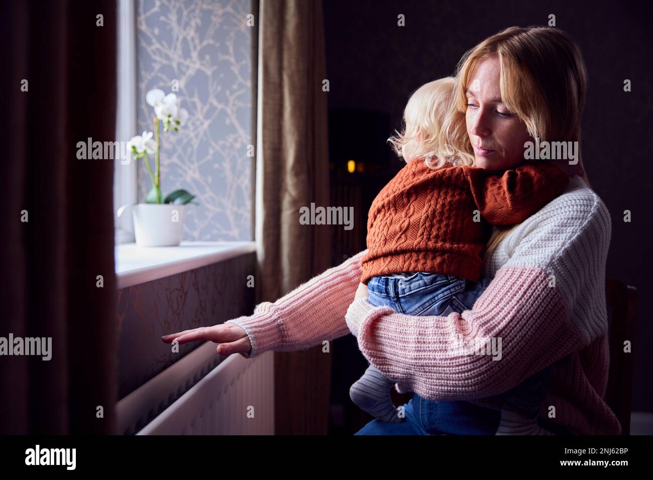 Mère avec fils essayant de rester au chaud par radiateur à la maison pendant la crise énergétique du coût de la vie Banque D'Images