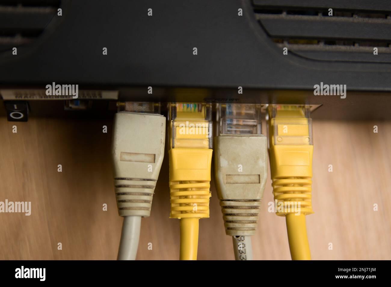 Gros plan de certains câbles de type ethernet RJ45 multicolores connectés à un routeur noir sur une table en bois Banque D'Images