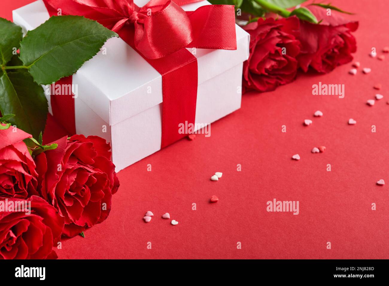 Concept dîner romantique. Décor romantique de table, argenterie, verres à vin, boîte cadeau, roses et symbole de l'amour coeur rouge sur fond rouge. Saint-Valentin Banque D'Images