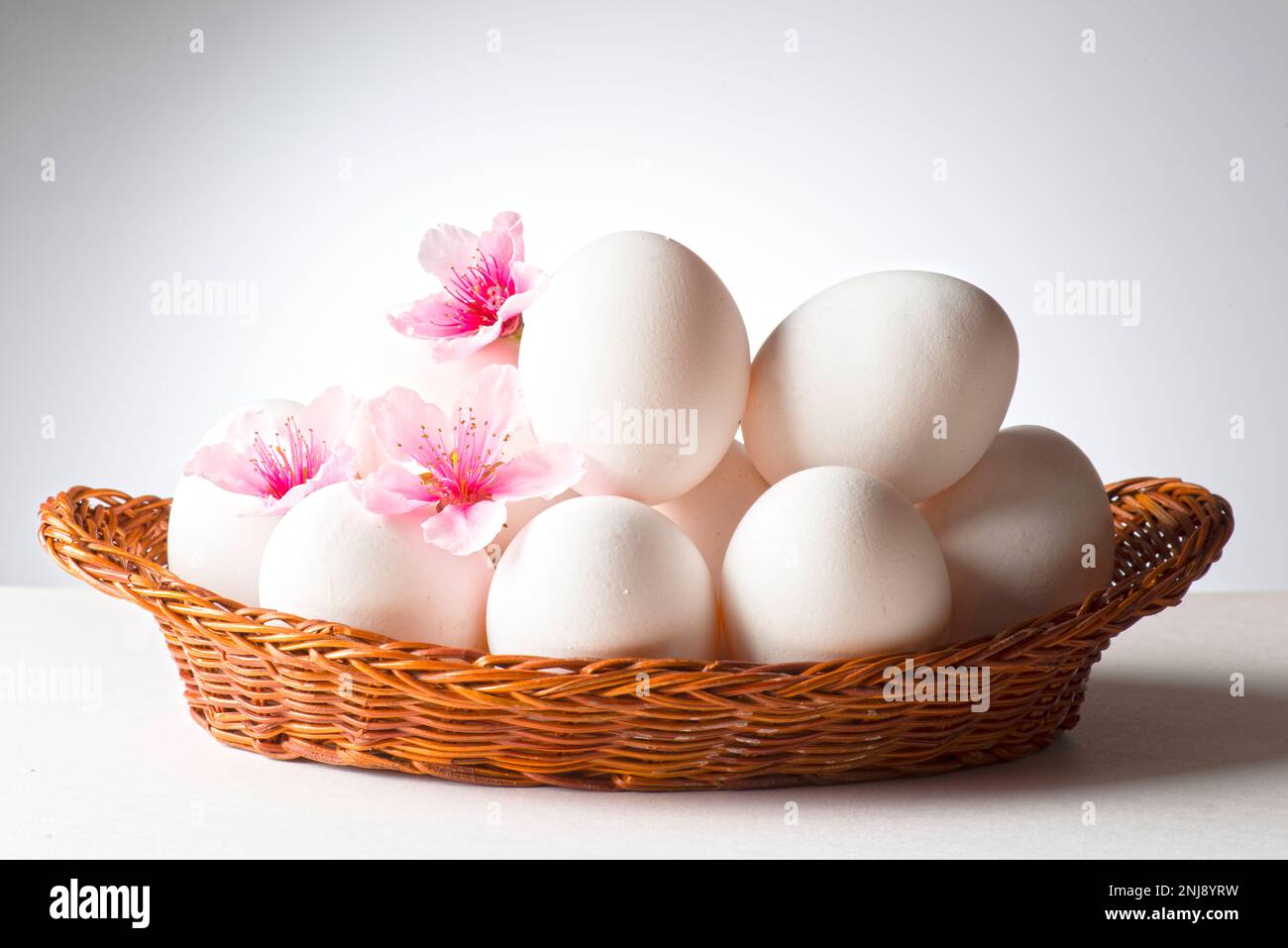 panier avec œufs blancs et fleurs de pêche Banque D'Images
