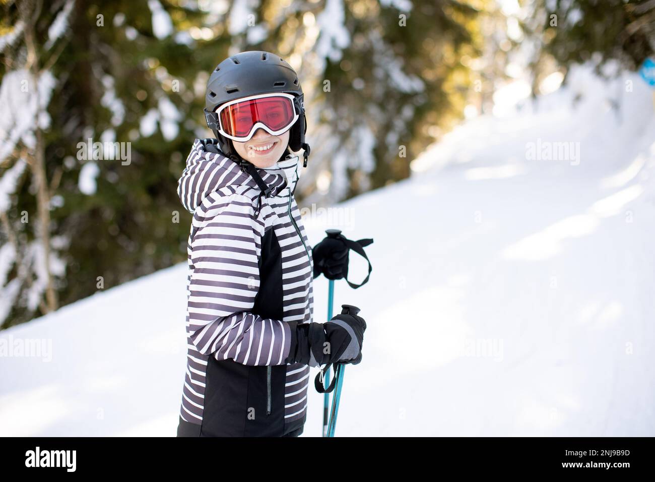 Jeune femme qui profite de la journée d'hiver pour skier sur les pistes enneigées, entourée de grands arbres et habillée pour les températures froides Banque D'Images