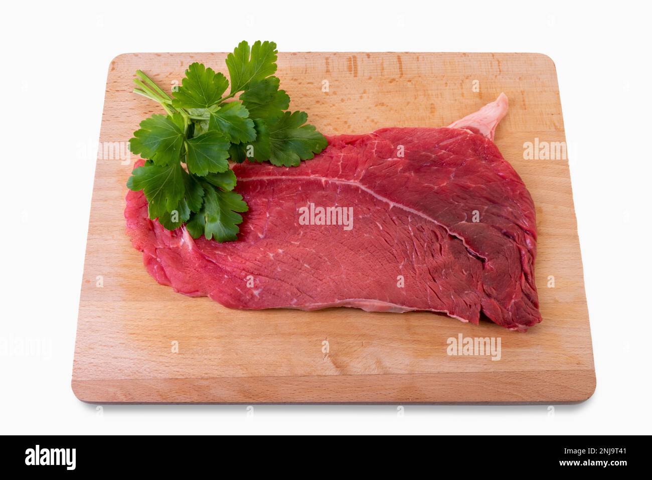 Steak de bœuf cru sur planche à découper en bois avec feuilles de persil isolées sur blanc avec passe-cheveux Banque D'Images