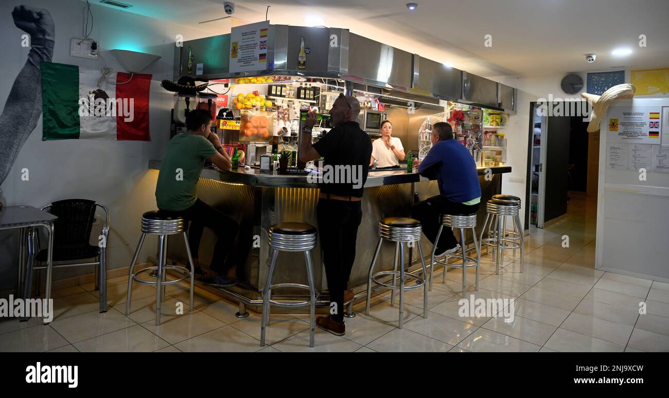 Bar avec clients assis sur des tabourets et femme derrière le comptoir Banque D'Images Bar avec clients assis sur des tabourets et femme derrière le comptoir Banque D'Images