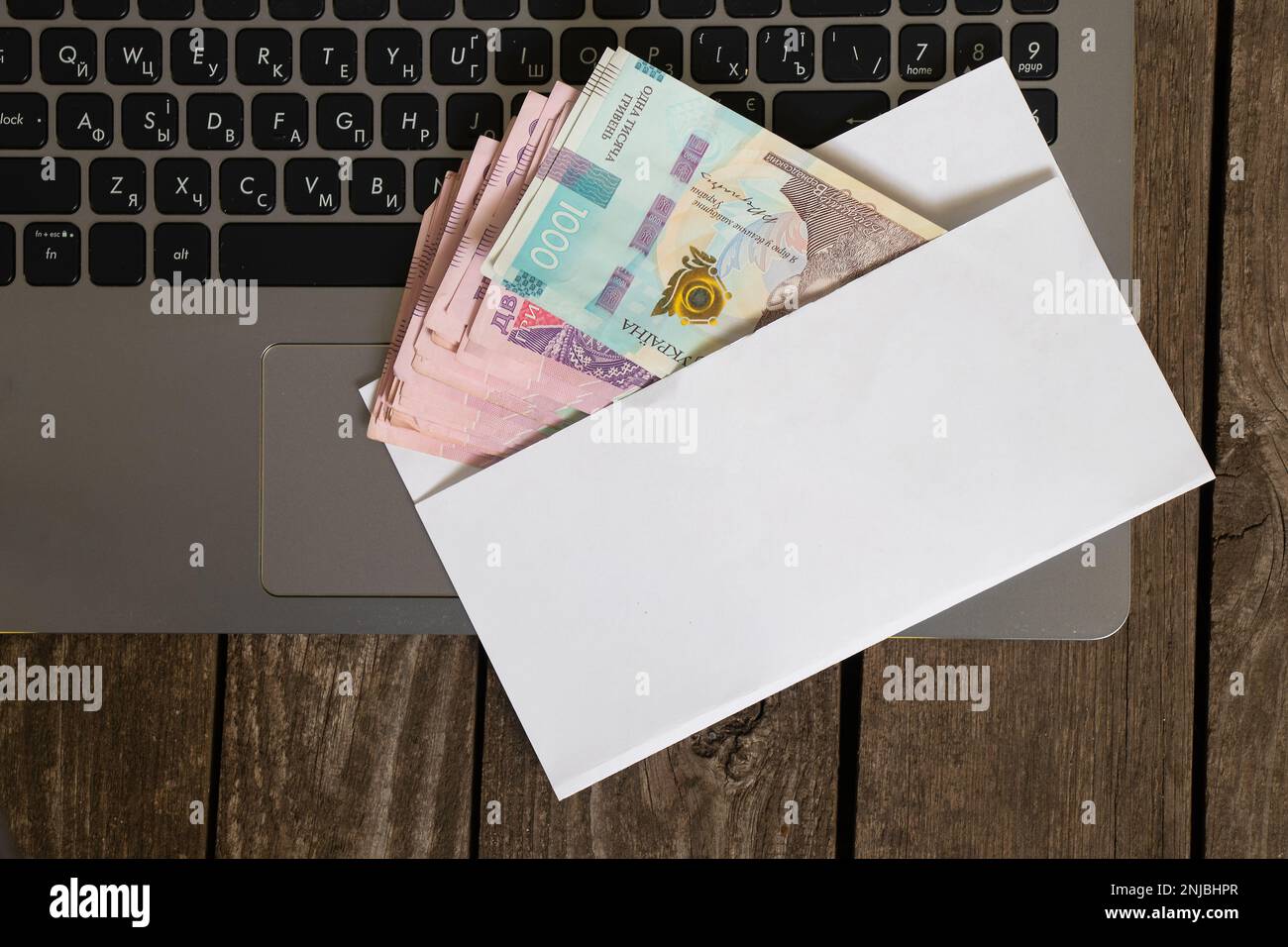 La monnaie ukrainienne se trouve dans une enveloppe blanche sur un ordinateur portable sur une enveloppe en bois, le salaire dans une enveloppe Banque D'Images