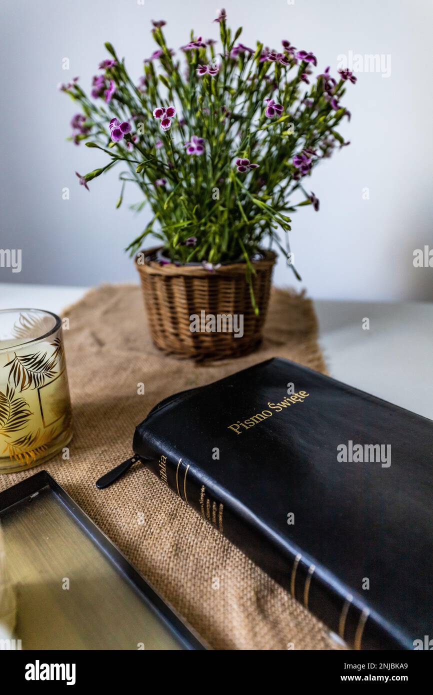 La Sainte Bible à couverture noire se trouve sur une table en bois à côté des fleurs et des petites bougies Banque D'Images