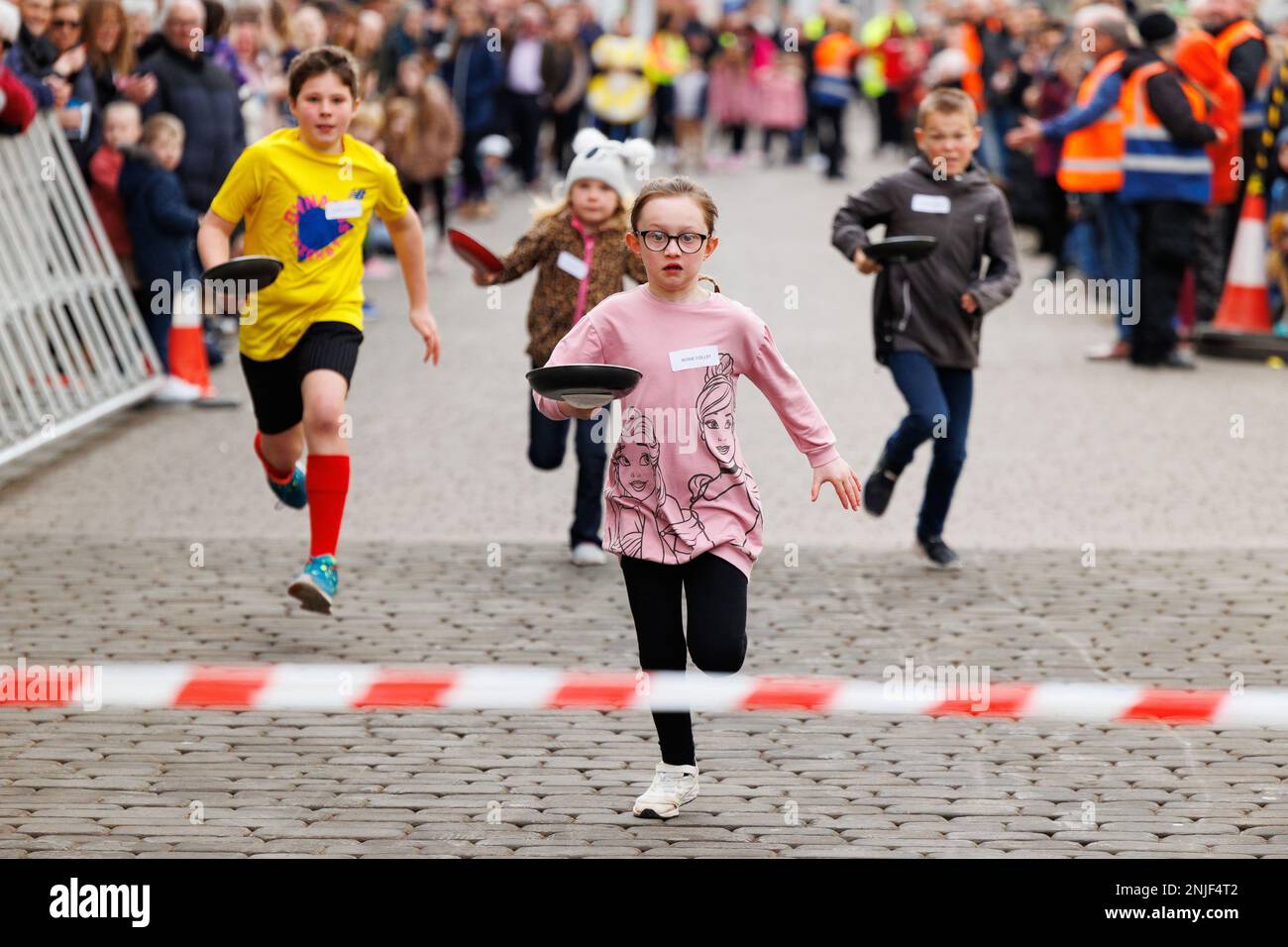 La course annuelle de crêpes Shrove Tuesday s'est tenue à Lichfield, Staffordshire, en Angleterre. L'événement comprend des courses pour enfants, une course de mascotte et des courses pour hommes et femmes. L'événement commence à midi et est accompagné par le crieur de la ville et jugé par le Seigneur Maire. Photo centre portant des lunettes, vainqueur des courses pour enfants Rosie Colley. Banque D'Images