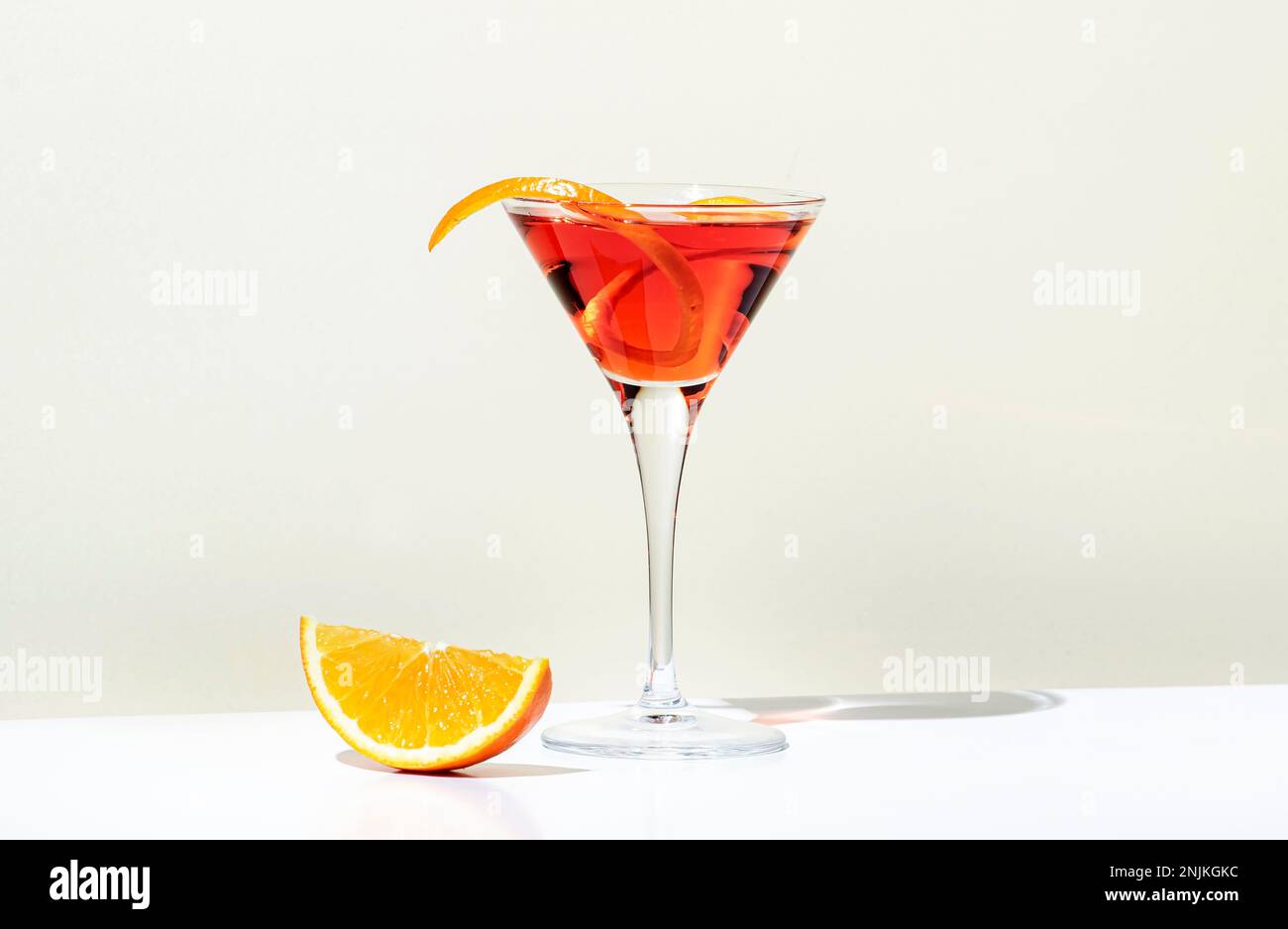 Boisson alcoolisée Martinez avec vermouth rouge, liqueur, orange amère, zeste et glace. Fond beige clair, lumière dure, motif ombre. Minimale Banque D'Images