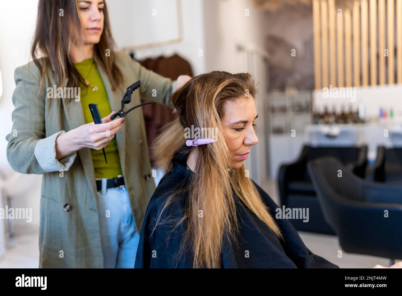 Coiffeur axé sur la récolte dans des vêtements décontractés divisant les cheveux de la cliente femelle en torons avant de colorer dans un studio de beauté moderne Banque D'Images
