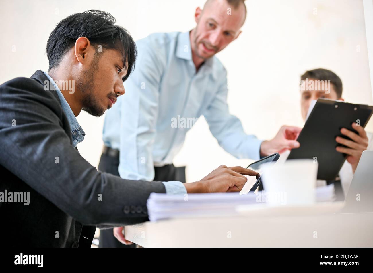 Un analyste financier masculin asiatique professionnel et intelligent du millénaire est en réunion avec des patrons caucasiens. vue latérale Banque D'Images