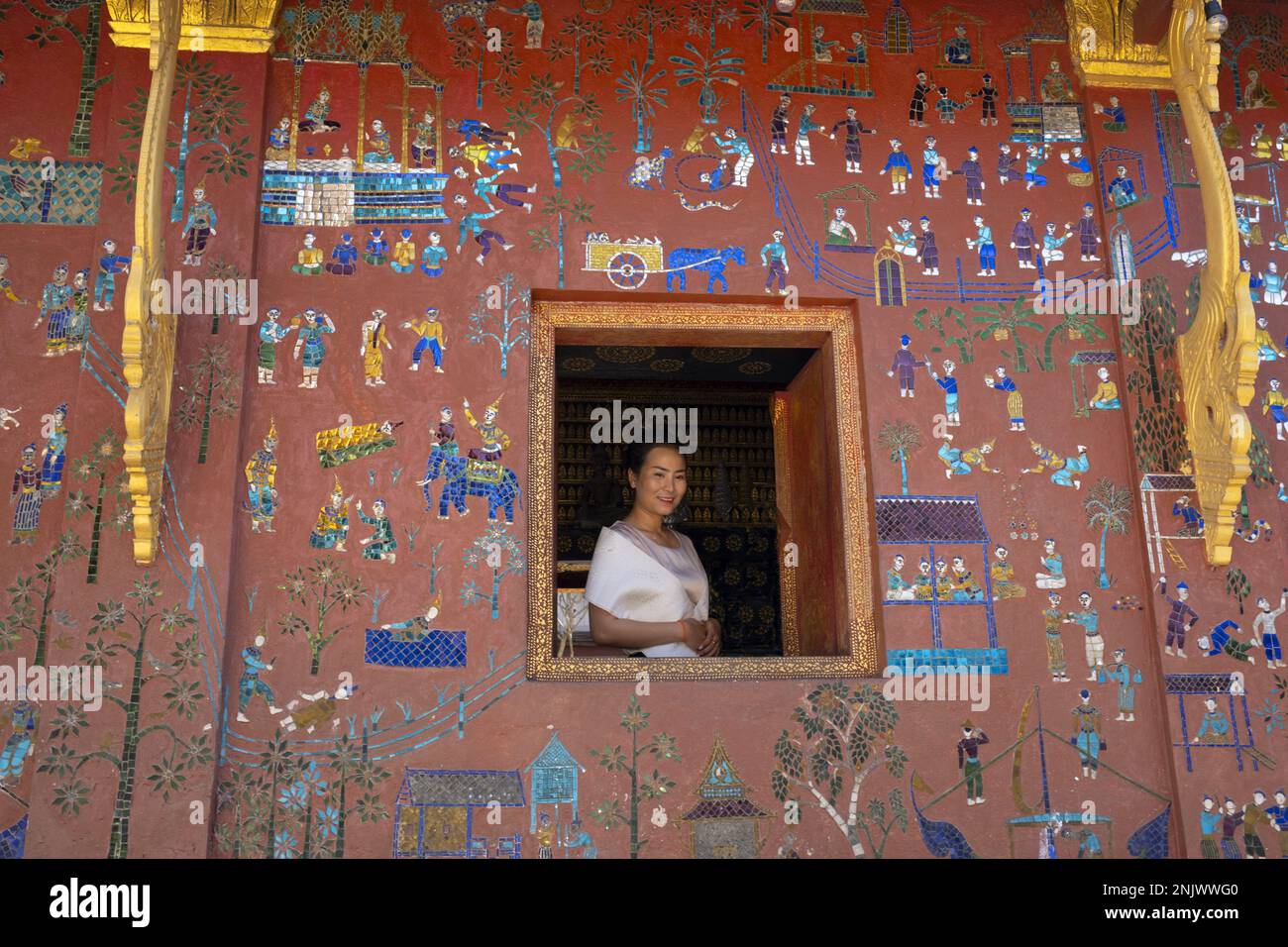 Laos: Une femme à une fenêtre dans la Chapelle Rouge, Wat Xieng Thong (Temple de la ville d'or), Luang Prabang. Wat Xieng Thong, avec ses toits surbaissés qui incarnent le style classique de Luang Prabang, a été construit en 1560 par le roi Setthathirat (1548–71) et a été condescendant par la monarchie jusqu'en 1975. Luang Prabang était autrefois la capitale d'un royaume du même nom. Jusqu'à la prise de pouvoir communiste en 1975, c'était la capitale royale et le siège du gouvernement du Royaume du Laos. La ville est aujourd'hui un site classé au patrimoine mondial de l'UNESCO. Banque D'Images