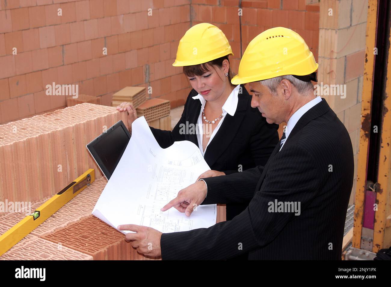 deux architectes avec ordinateur portable, plan de construction et niveau d'eau sur le chantier de construction Banque D'Images