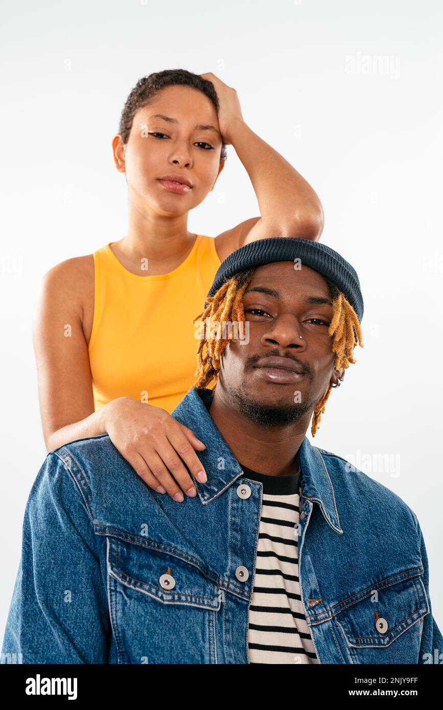 Positive mixte race femme avec les cheveux courts en Jean et orange haut appuye sur le dos de l homme en veste de denim sur fond blanc regardant l appareil photo Photo Stock