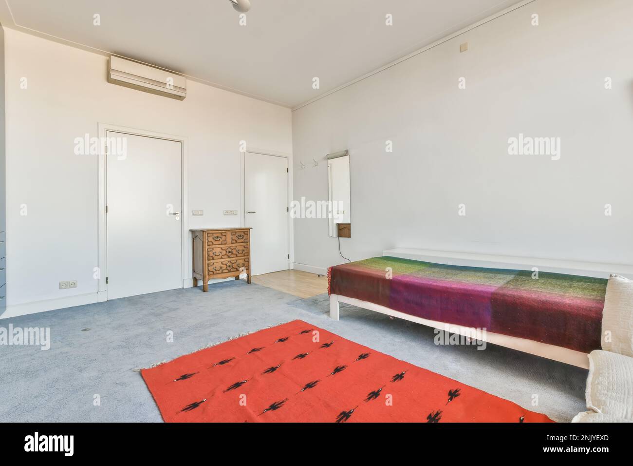 Décoration intérieure de chambre spacieuse avec moquette au sol et tapis rouge près d'un lit simple avec miroir suspendu au mur blanc Banque D'Images