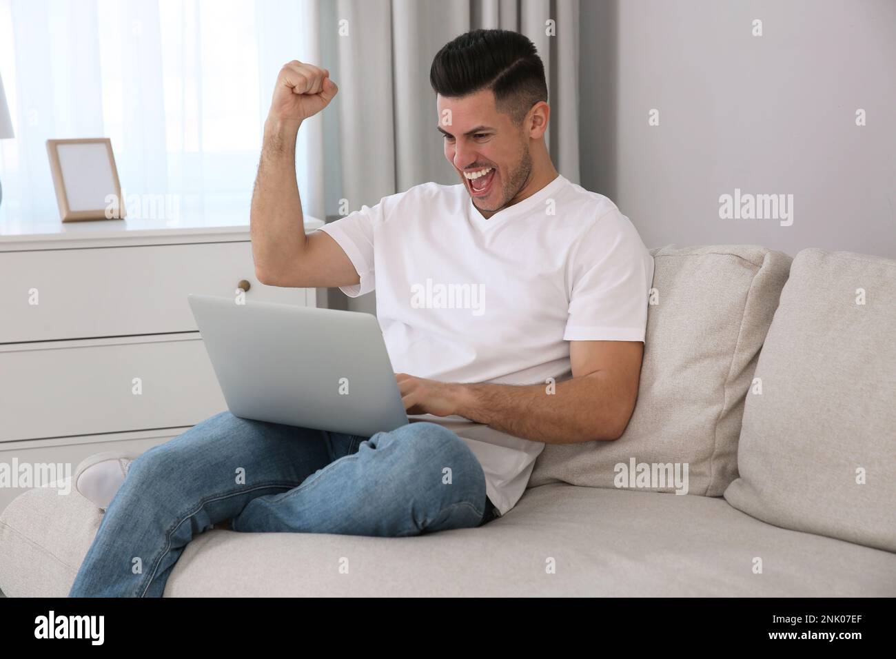 Homme émotionnel participant à la vente aux enchères en ligne à l'aide d'un ordinateur portable à la maison Banque D'Images