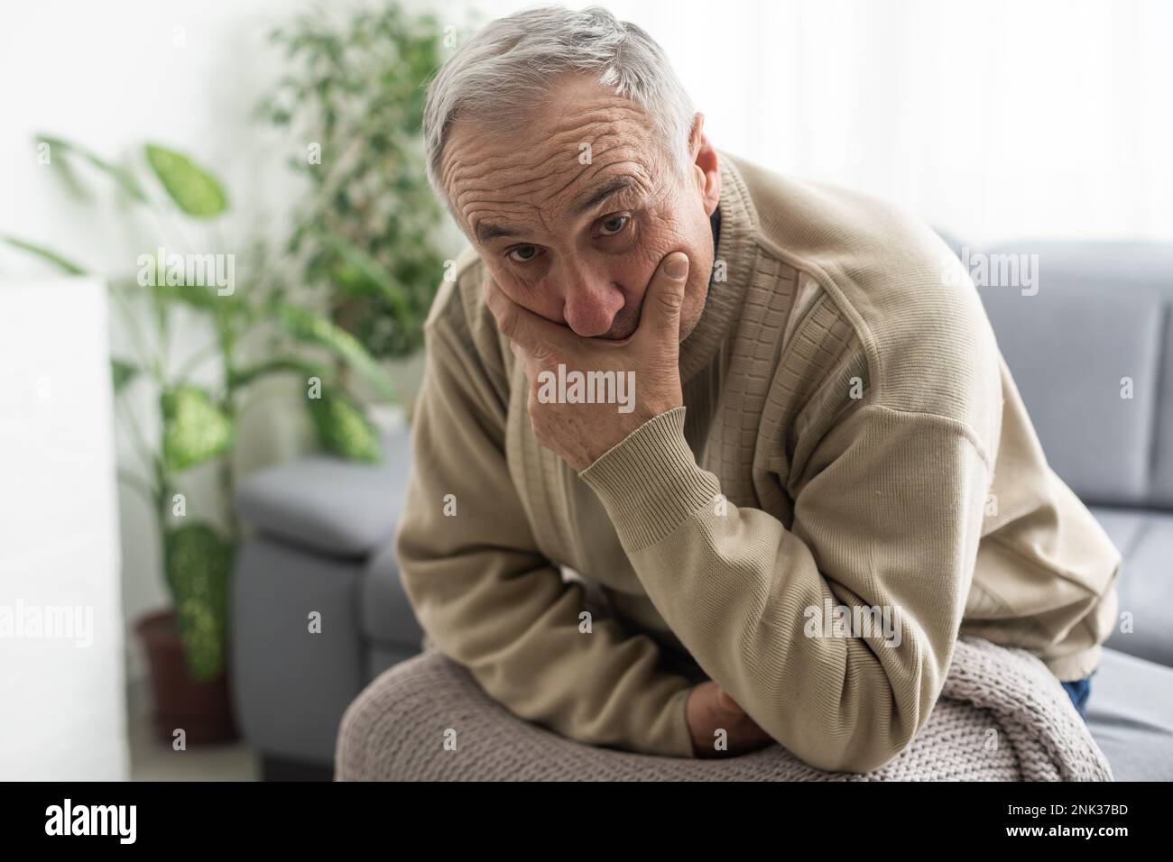 Frustré malheureux d'âge moyen mature homme assis sur le canapé, se sentant déprimé seul à la maison. Un grand-père à la retraite à la fois confus et troublé Banque D'Images