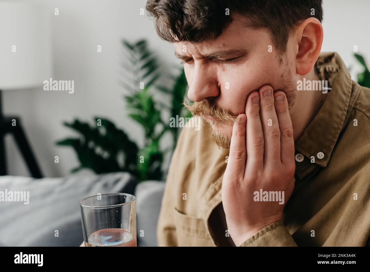 Triste homme caucasien 30s s'asseoir sur le canapé à la maison touchant la joue, se sentir blessé et souffrant de douleur sensible de dent. Concept de douleur et de cavités. Jeune contrarié Banque D'Images
