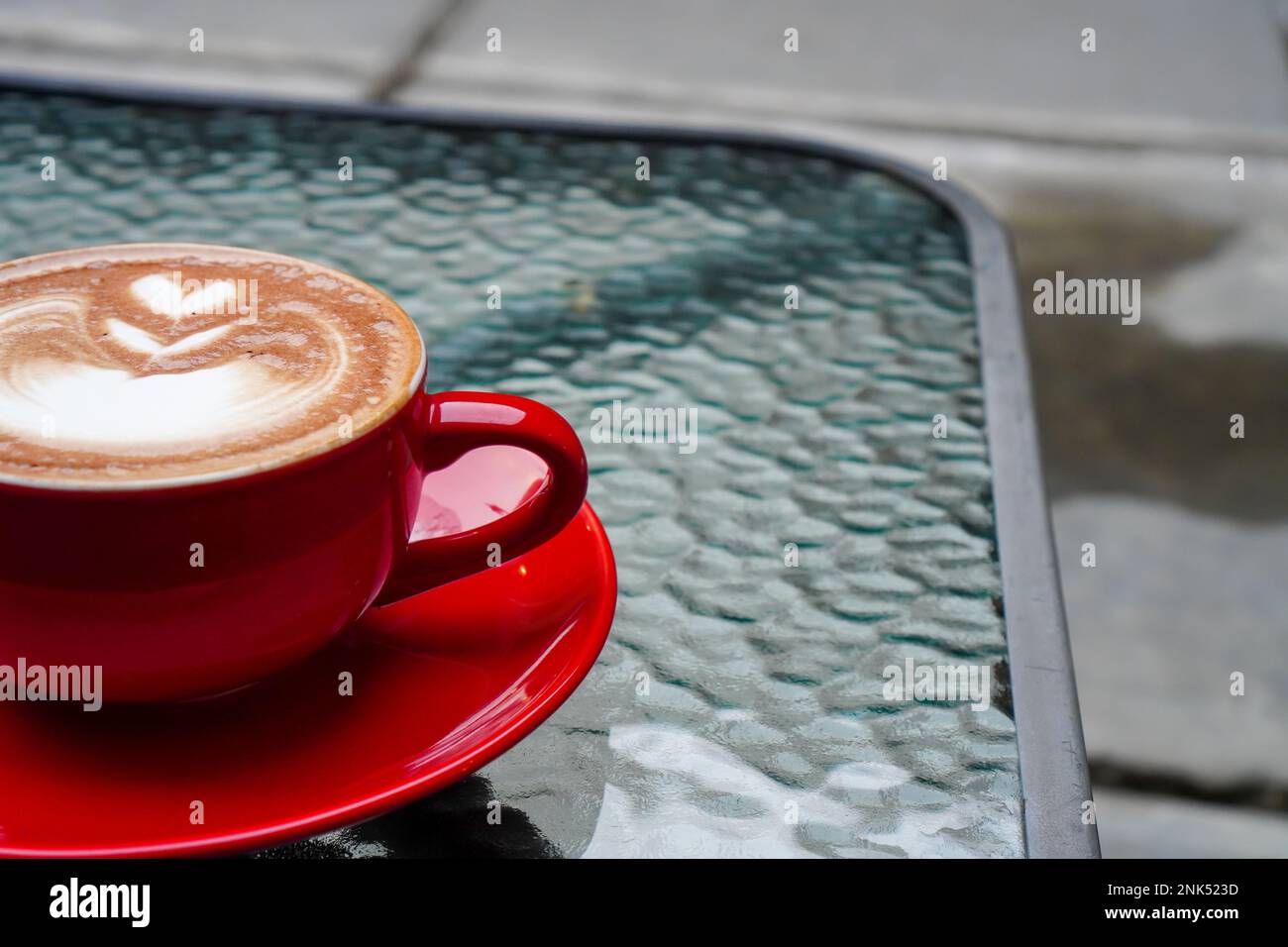 Une photo d'une demi-tasse de cappuccino. Cappuccino dans une tasse rouge servi sur une table en verre Banque D'Images