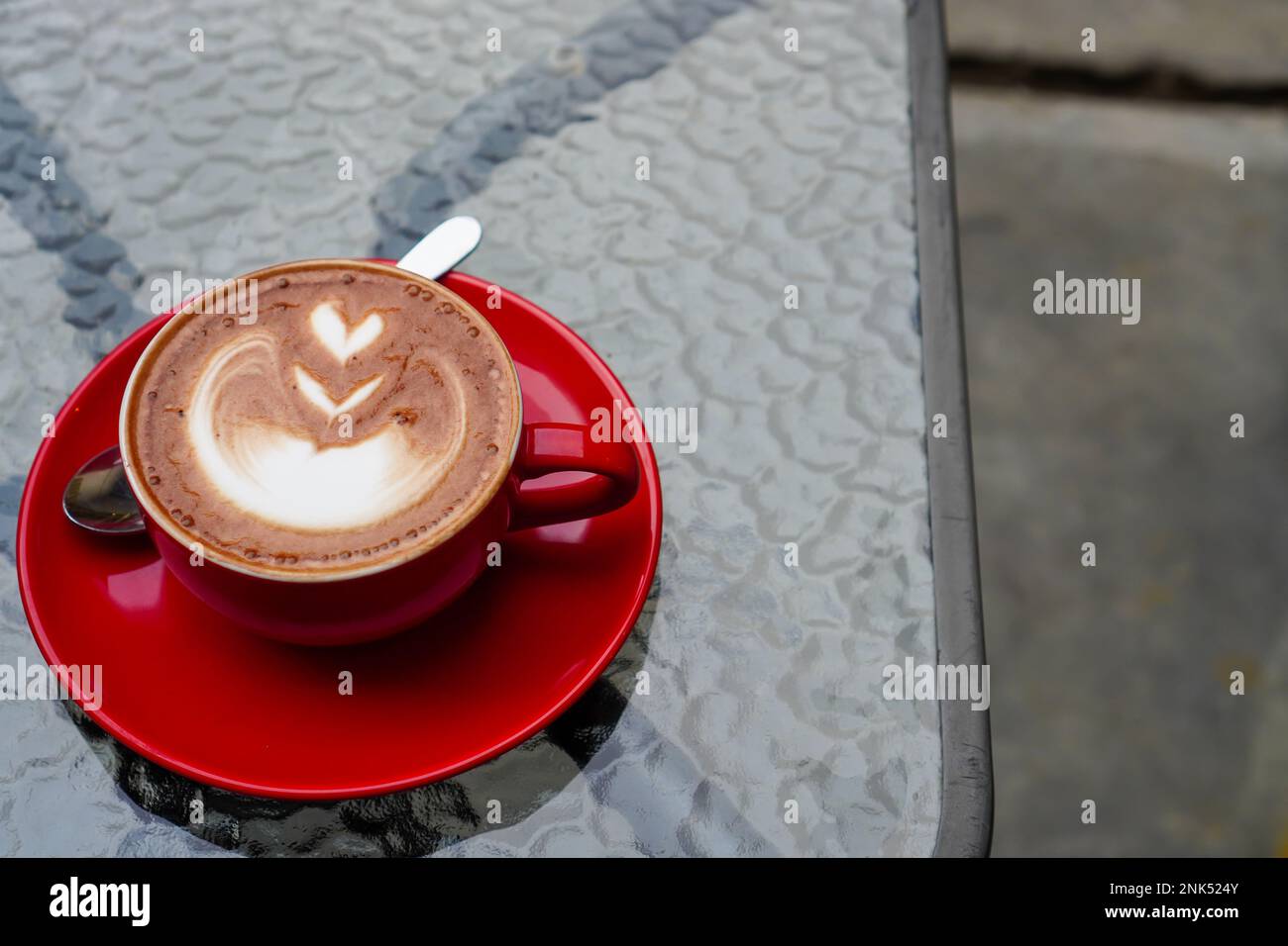 Une photo d'une demi-tasse de cappuccino. Cappuccino dans une tasse rouge servi sur une table en verre avec espace de copie Banque D'Images