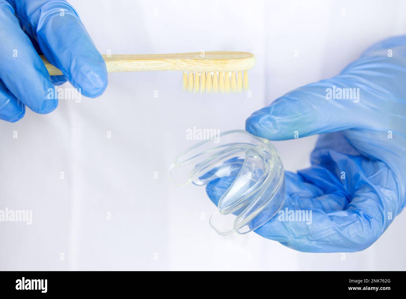 Gros plan de médecins mains dans des gants tenant le protège-bouche en silicone avec une brosse à dents en bois. Soins des dents. Banque D'Images