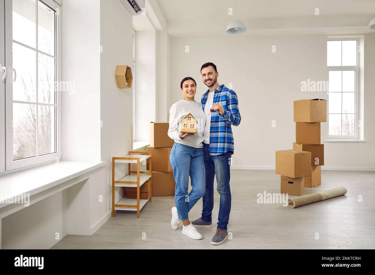 Photo pleine grandeur d'un couple heureux marié tenant les clés de leur nouvel appartement spacieux et moderne et maquette de maison de jouet. Un couple familial regarde dans l'appareil photo Banque D'Images