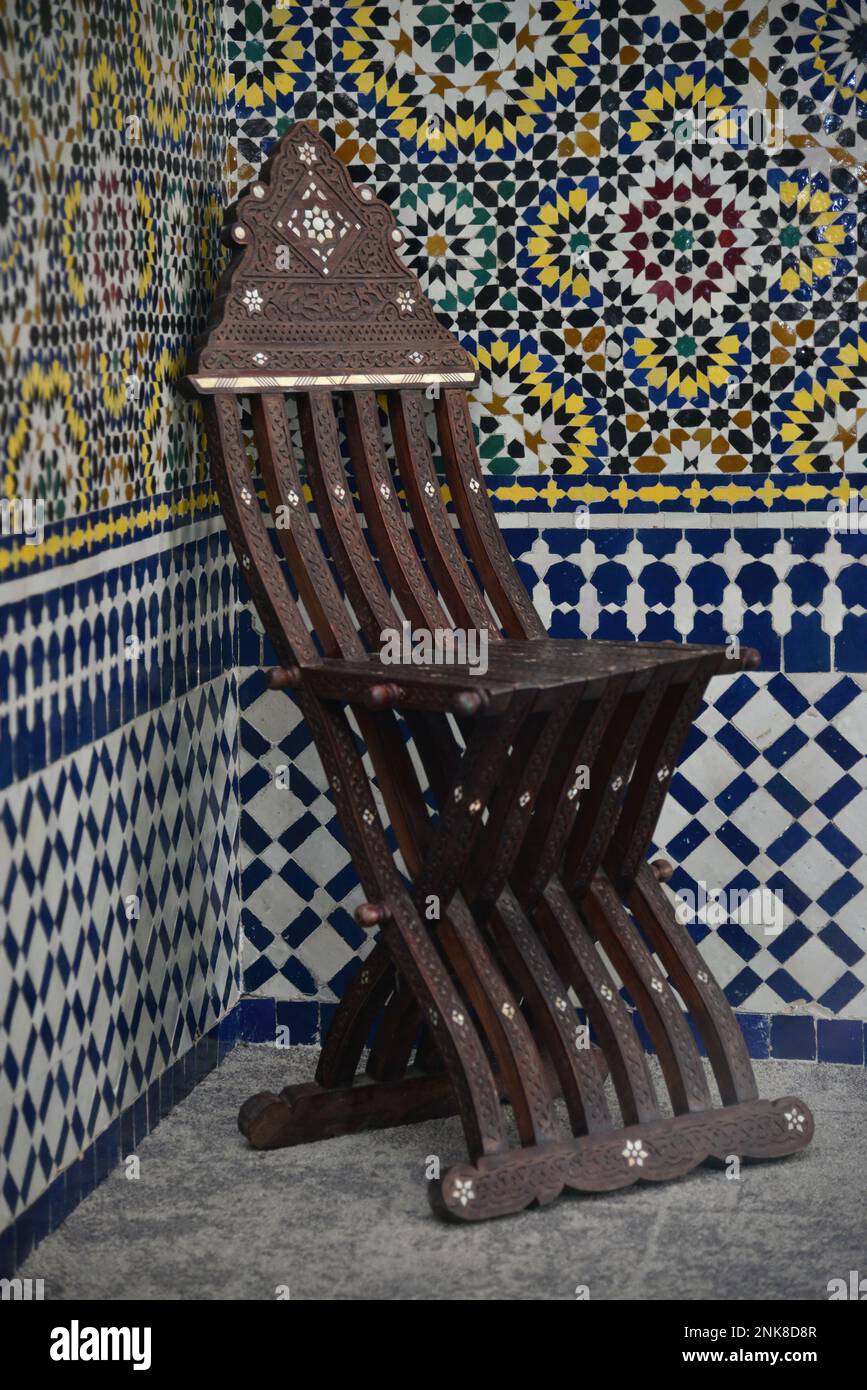 Une ancienne chaise marocaine en bois devant un mur de zellij marocain