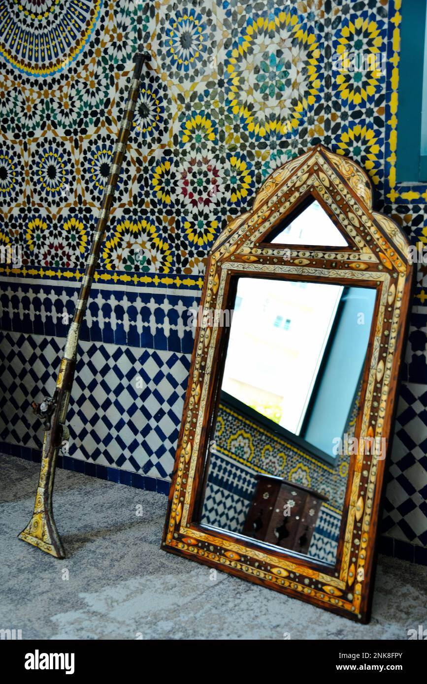 Un fusil marocain avec un vieux miroir à côté d'un mur de zellij marocain traditionnel Banque D'Images