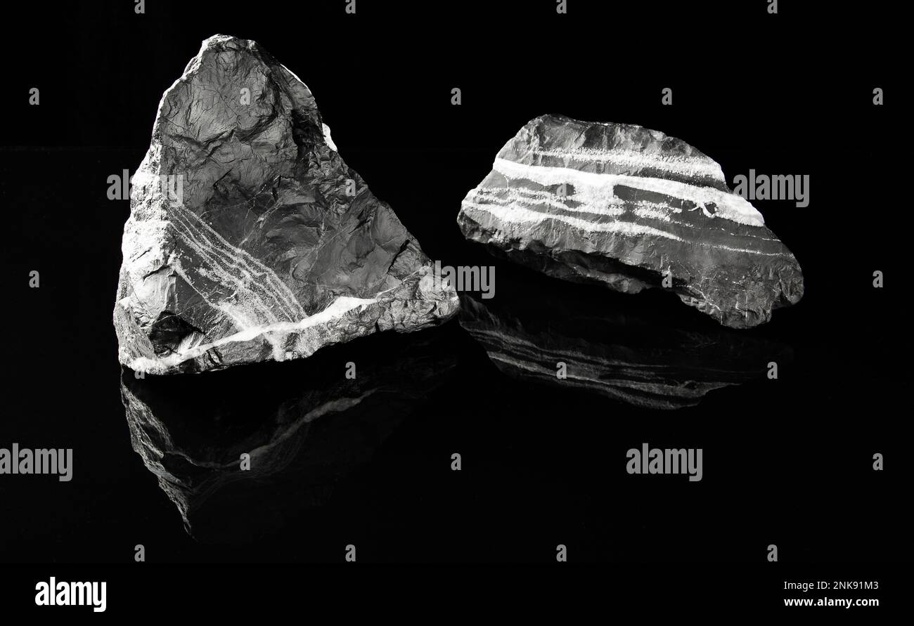 Minimalisme, pierres décoratives à rayures noires et blanches pour la décoration d'aquarium sur fond noir sont reflétées dans une surface miroir noire. Banque D'Images