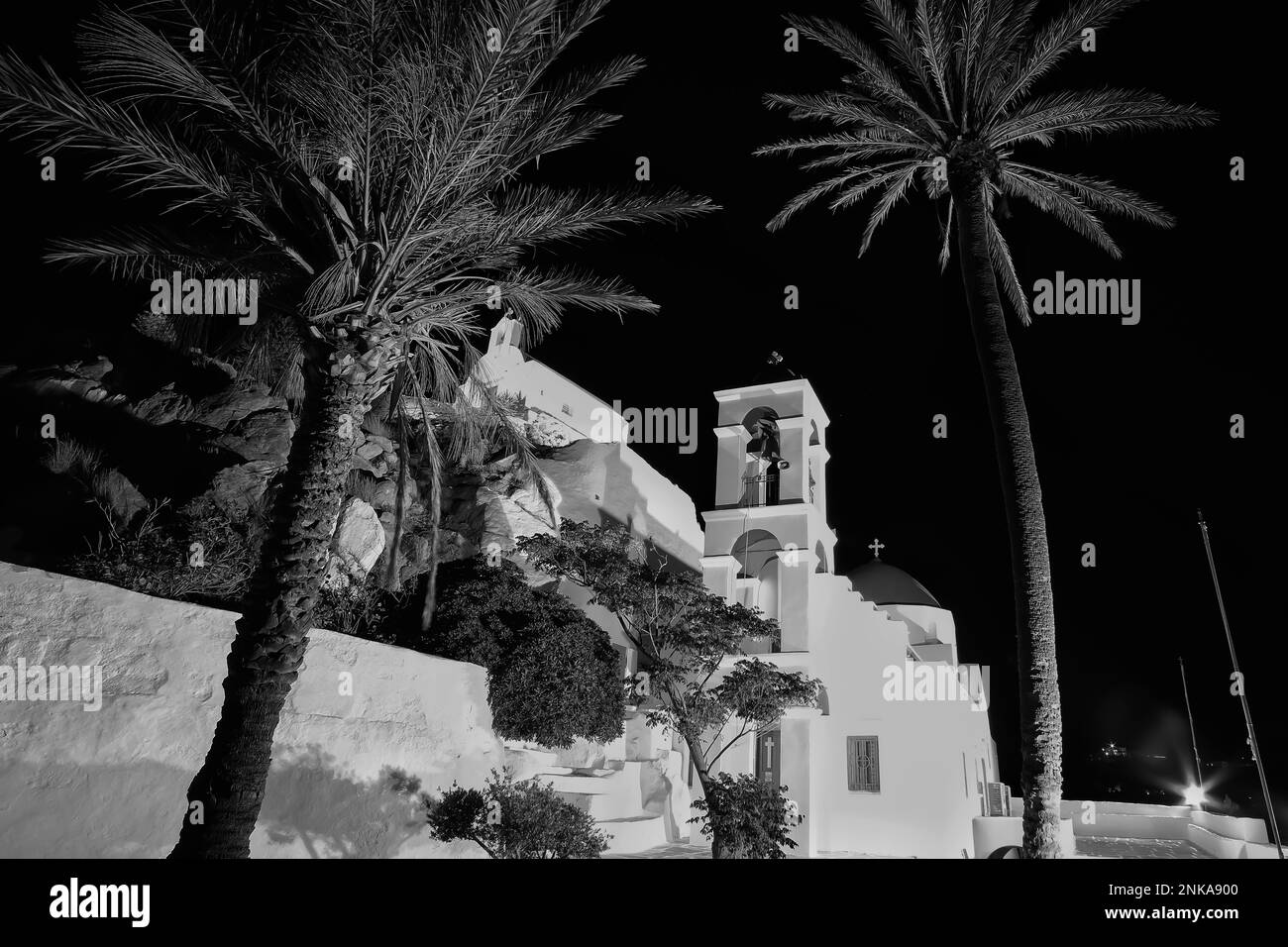L'église orthodoxe blanchie à la chaux illuminée de Panagia Gremniotissa à iOS Grèce, entourée de palmiers la nuit en noir et blanc Banque D'Images