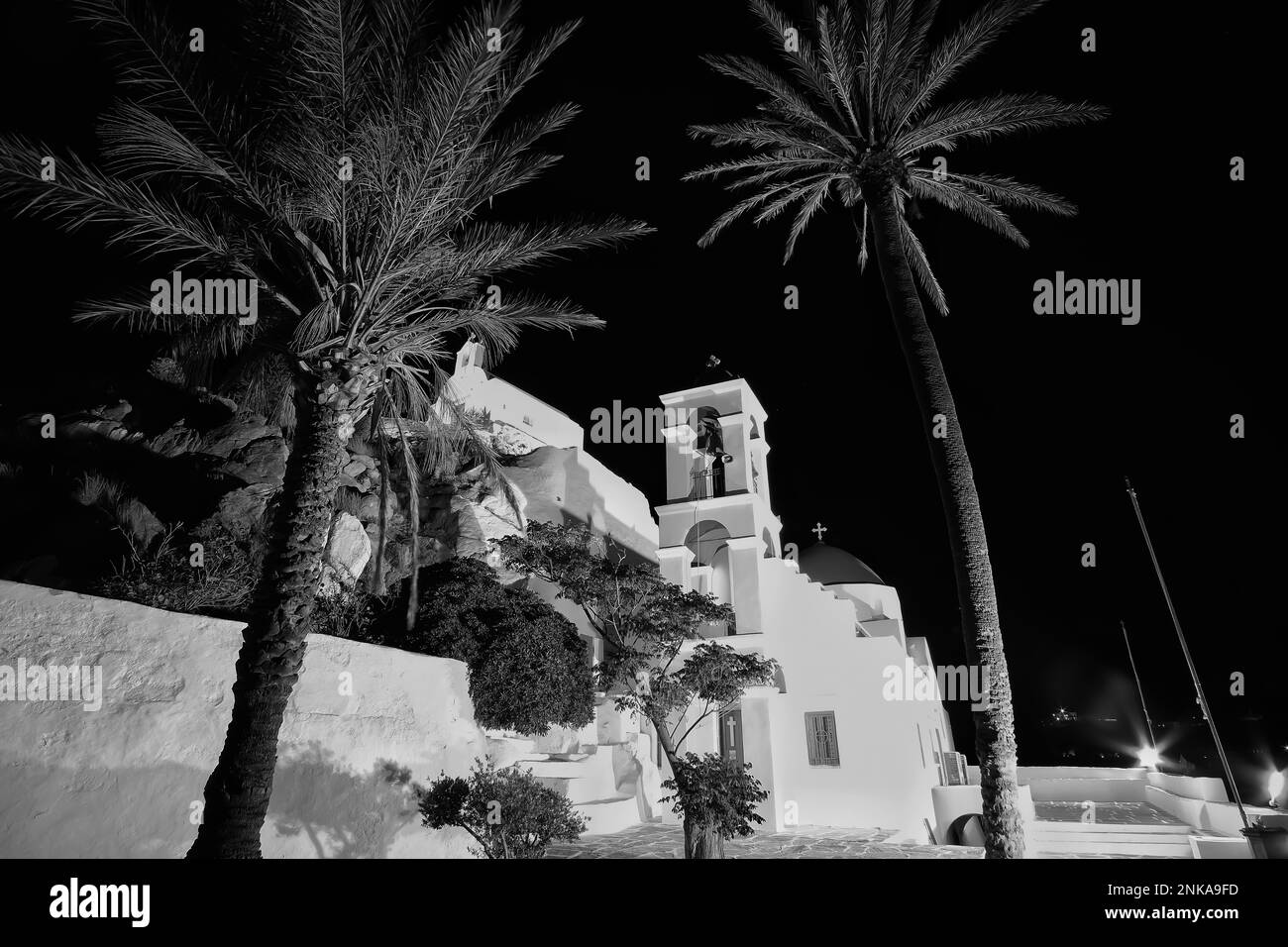 L'église orthodoxe blanchie à la chaux illuminée de Panagia Gremniotissa à iOS Grèce, entourée de palmiers la nuit en noir et blanc Banque D'Images