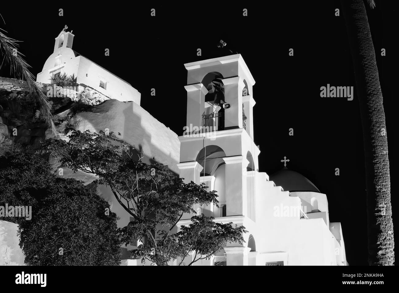 L'église orthodoxe blanchie à la chaux illuminée de Panagia Gremniotissa à iOS Grèce, entourée de palmiers la nuit en noir et blanc Banque D'Images