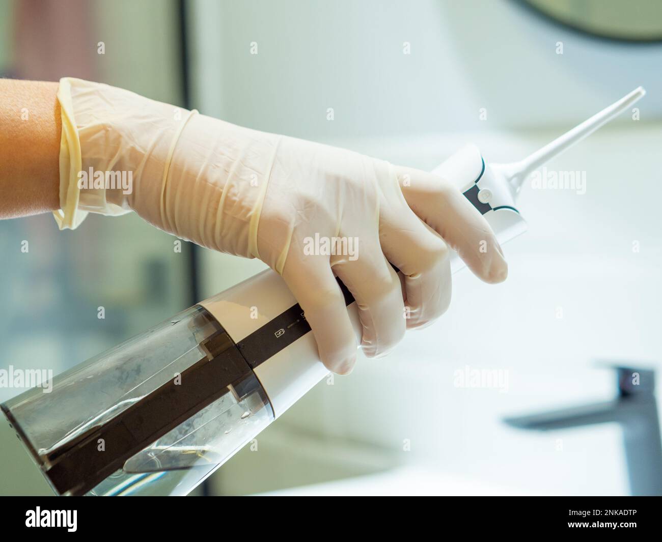 Main du dentiste montrant comment utiliser un démousseur d'eau dentaire domestique pour un nettoyage en profondeur à la maison Banque D'Images