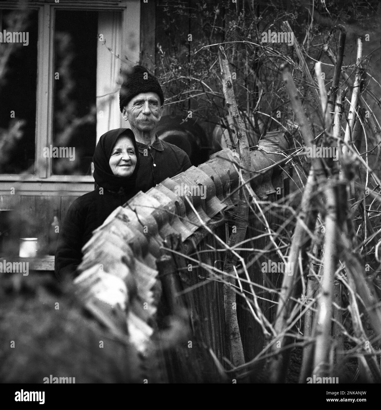 Comté de Suceava, République socialiste de Roumanie, env. 1980. Couple de personnes âgées vivant sur leur propriété rurale, posant derrière la clôture avec des cruches en céramique placées sur le dessus. Banque D'Images