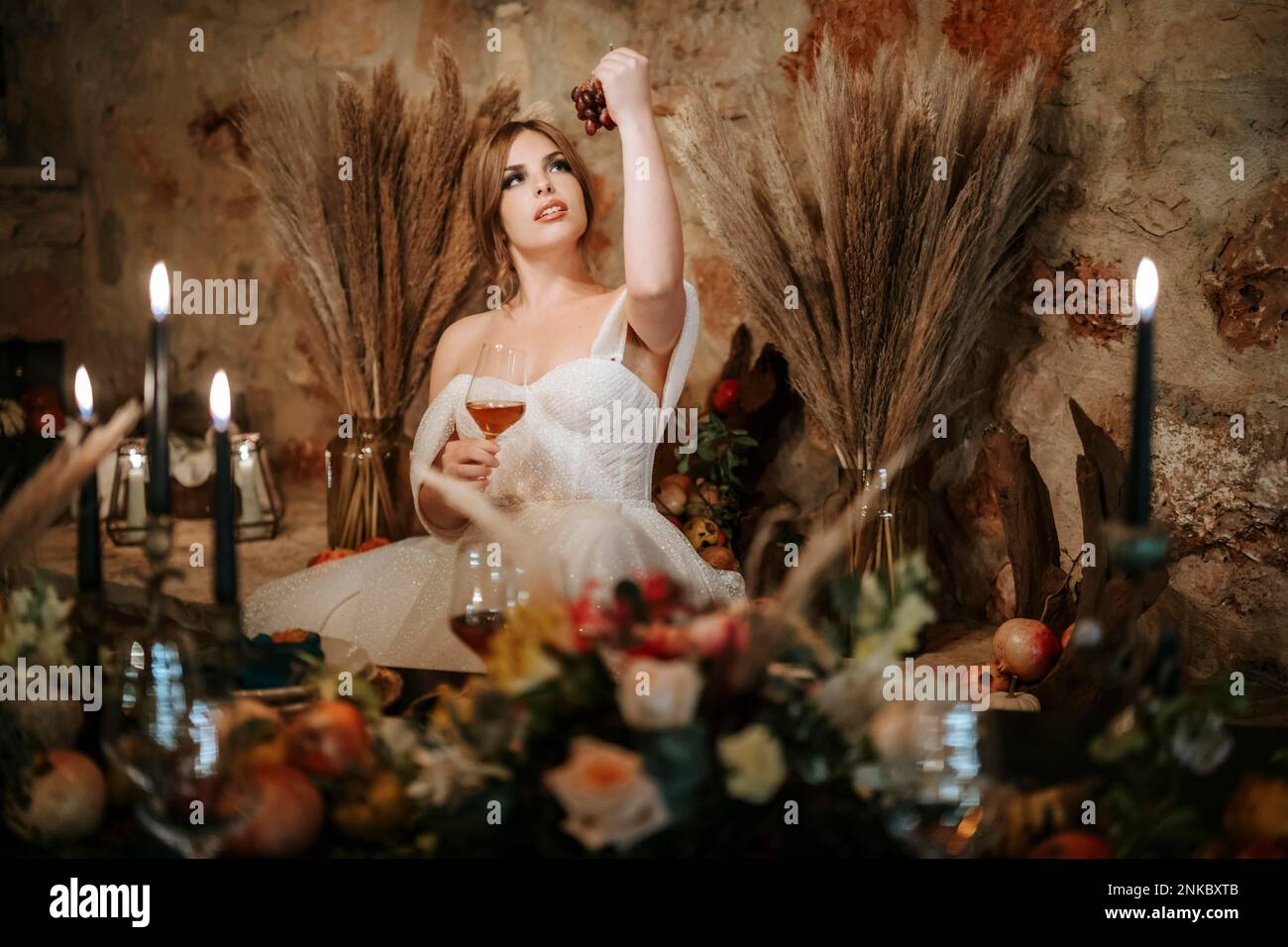 Belle mariée par table de mariage, richement décorée avec des fleurs et des bougies Banque D'Images