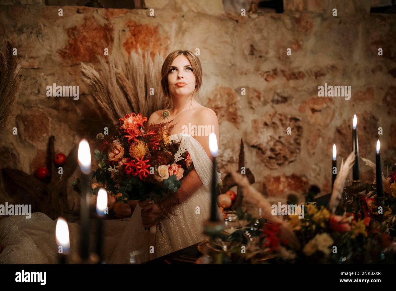 Belle mariée par table de mariage, richement décorée avec des fleurs et des bougies Banque D'Images