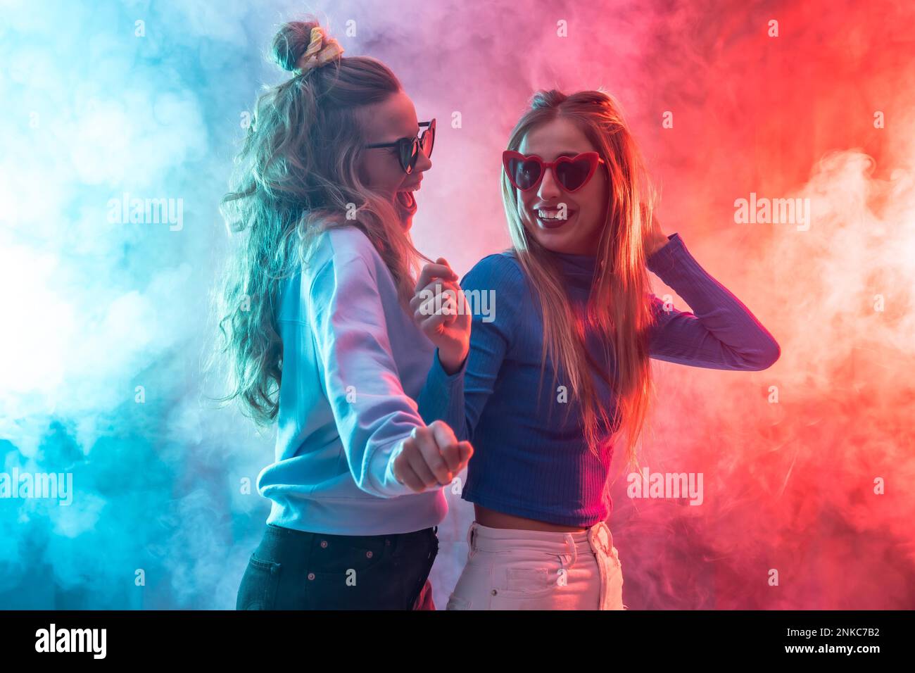 Deux jeunes femmes blanches blondes dansant dans la boîte de nuit, dansant s'amuser à la fête, rouge et bleu LED fumée Banque D'Images