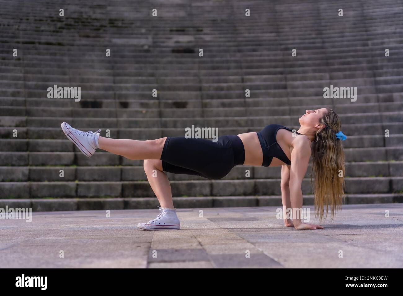 Jeune femme caucasienne faisant de la forme physique dans un parc de ville, squats pour travailler les jambes et les fesses Banque D'Images