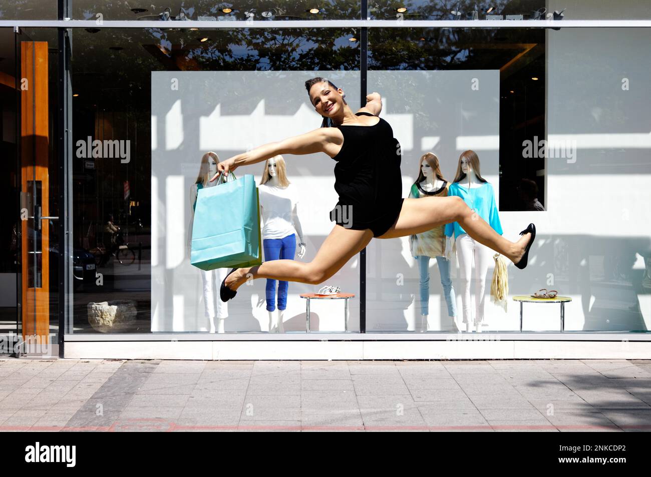 Une jeune femme sautant pour la joie devant un magasin Banque D'Images