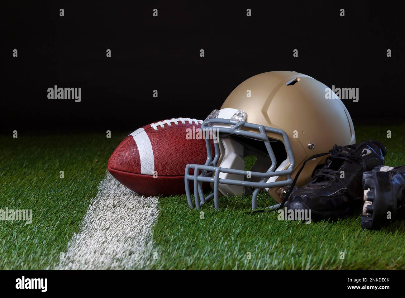 Casque de football avec ballon de football et crampons sur un terrain d'herbe avec une bande blanche et un fond sombre Banque D'Images