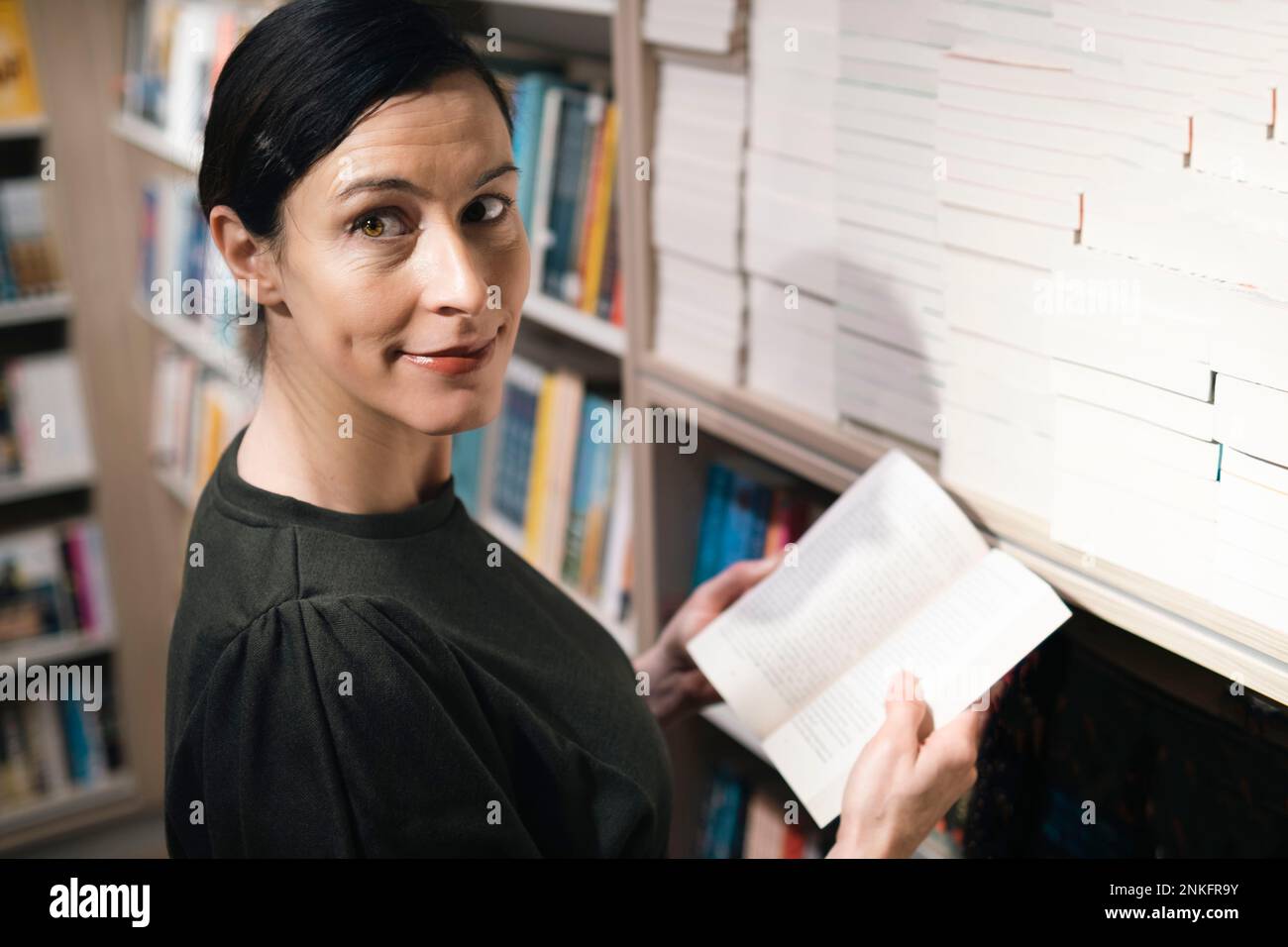 Un bibliothécaire souriant tient le livre devant la bibliothèque Banque D'Images